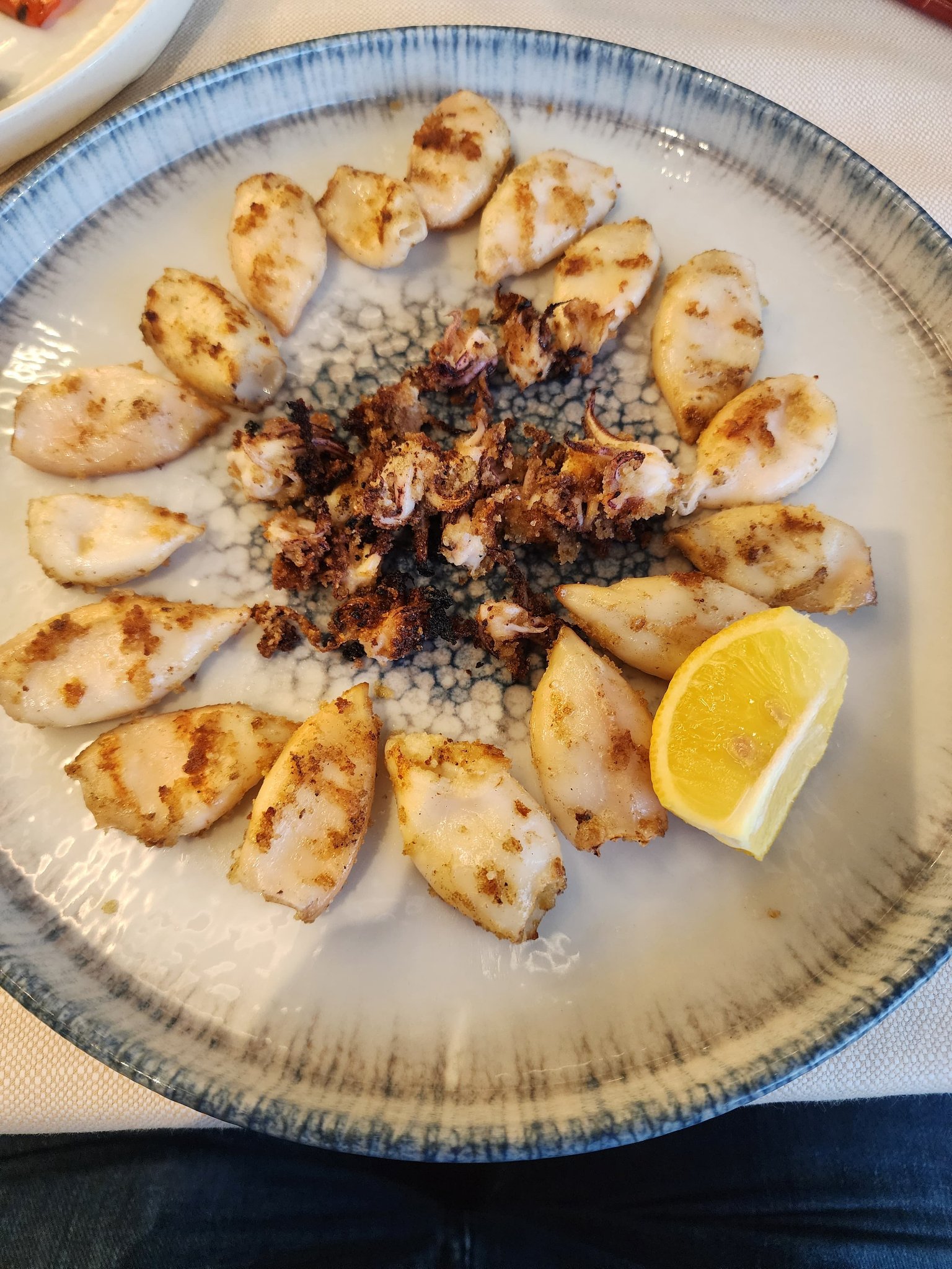 Grilled calamari arranged around a plate with a fresh lemon wedge